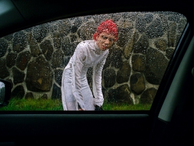 A boy peers through a car window directly at the viewer