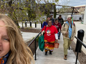 Milwaukee Riverkeeper Cheryl Nenn smiles in a selfie as walkers follow the Riverwalk with the Menomonee/Milwaukee confluence beyond